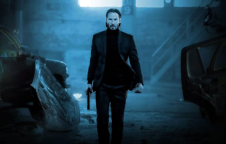 Man in a dark suit walking toward the camera in a ruined garage, holding a pistol in his right hand under blue-tinted lighting