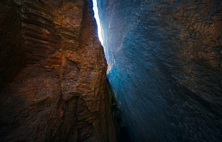 Narrow canyon shaft between rugged rock walls with bright sky visible overhead
