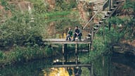 Loving father is teaching his son to catch fish on autumn day, people are sitting on wooden pier with rods and talking sharing experience. Recreation, nature and family concept.